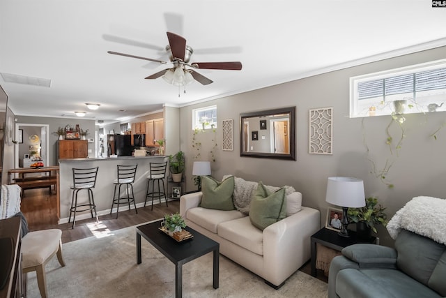 living room featuring crown molding, a ceiling fan, visible vents, and light wood-type flooring