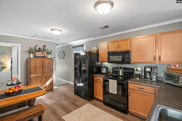 kitchen with dark countertops, visible vents, ornamental molding, light wood-style flooring, and black appliances