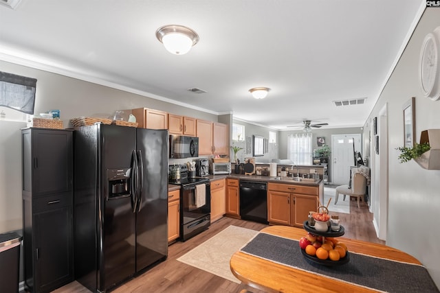 kitchen with visible vents, a peninsula, light wood-style floors, black appliances, and a sink