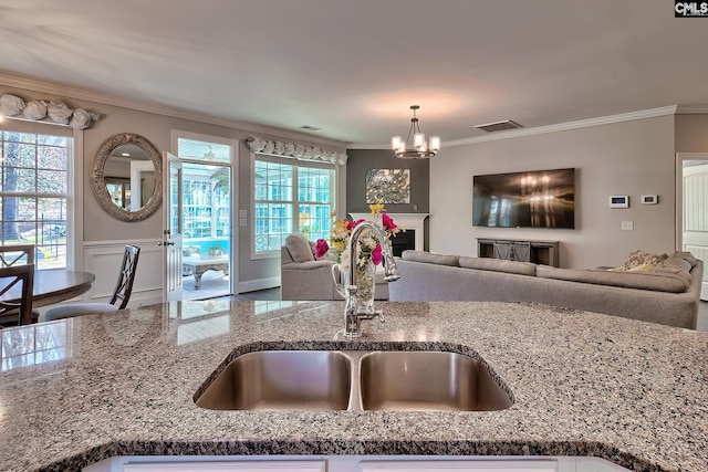 kitchen featuring ornamental molding, a sink, open floor plan, an inviting chandelier, and light stone countertops