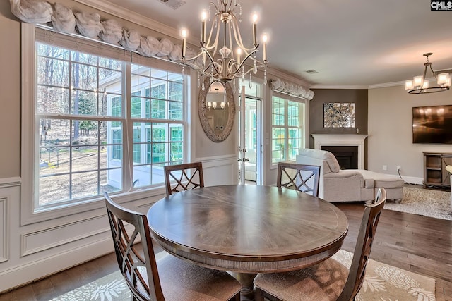 dining space featuring a notable chandelier, a fireplace, wood finished floors, and ornamental molding