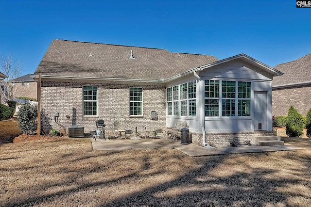 back of property with brick siding, cooling unit, a shingled roof, and a patio