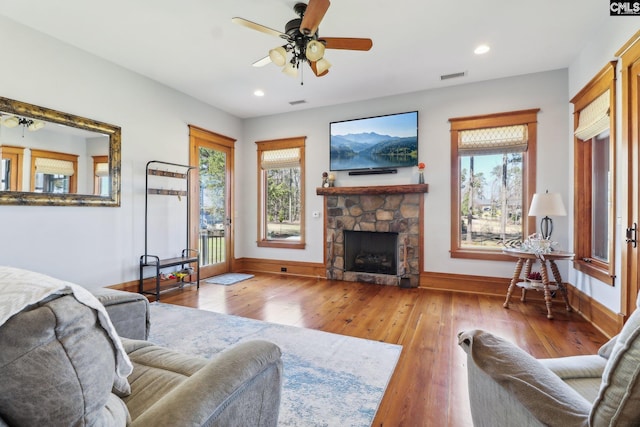 living area featuring a fireplace, hardwood / wood-style flooring, a healthy amount of sunlight, and ceiling fan