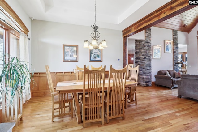 dining room with decorative columns, wainscoting, a raised ceiling, a notable chandelier, and light wood-type flooring