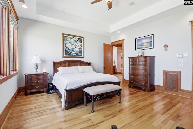 bedroom with a tray ceiling, visible vents, and light wood finished floors