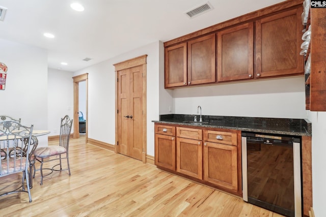 kitchen featuring beverage cooler, brown cabinetry, visible vents, light wood-style flooring, and a sink