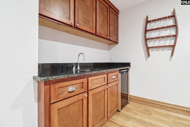 bar featuring baseboards, light wood finished floors, a sink, indoor wet bar, and dishwasher