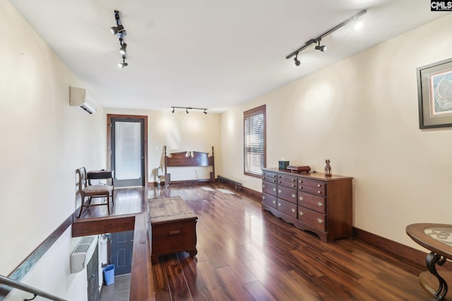 bedroom with baseboards, an AC wall unit, wood finished floors, and rail lighting