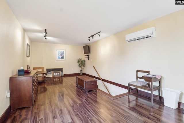 sitting room with a wall unit AC, rail lighting, baseboards, and dark wood-style flooring