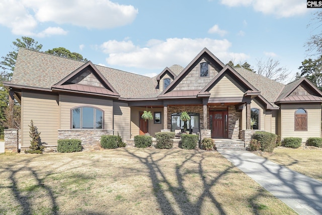 craftsman-style house featuring a standing seam roof, a front yard, stone siding, and metal roof