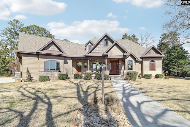 craftsman-style house featuring a standing seam roof, stone siding, a shingled roof, and a front lawn