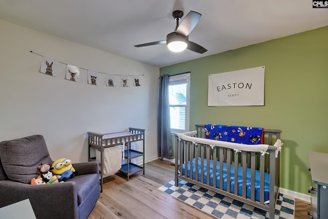 bedroom featuring baseboards, a crib, wood finished floors, and a ceiling fan