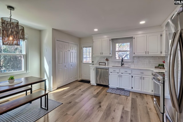 kitchen with light wood-style flooring, a sink, light countertops, appliances with stainless steel finishes, and a chandelier