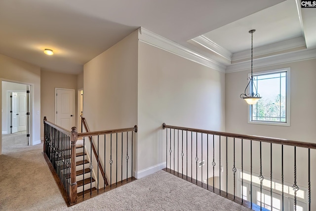 hallway featuring baseboards, a tray ceiling, crown molding, carpet flooring, and an upstairs landing