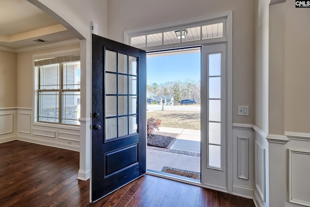 foyer entrance with dark wood-style floors, a wainscoted wall, visible vents, arched walkways, and a decorative wall