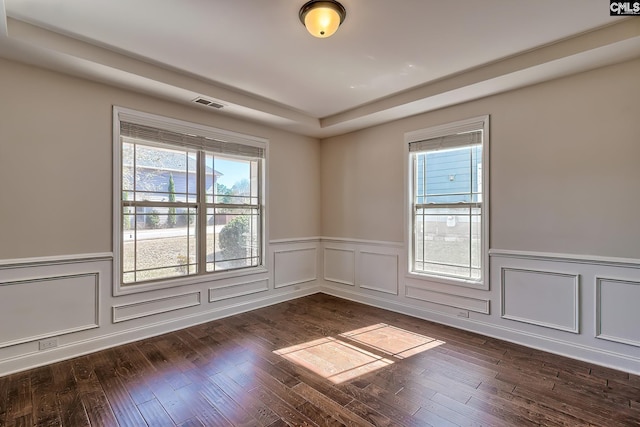 spare room with dark wood finished floors, a wainscoted wall, visible vents, and a tray ceiling