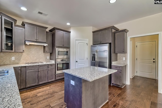 kitchen featuring under cabinet range hood, light stone counters, dark wood-type flooring, and appliances with stainless steel finishes