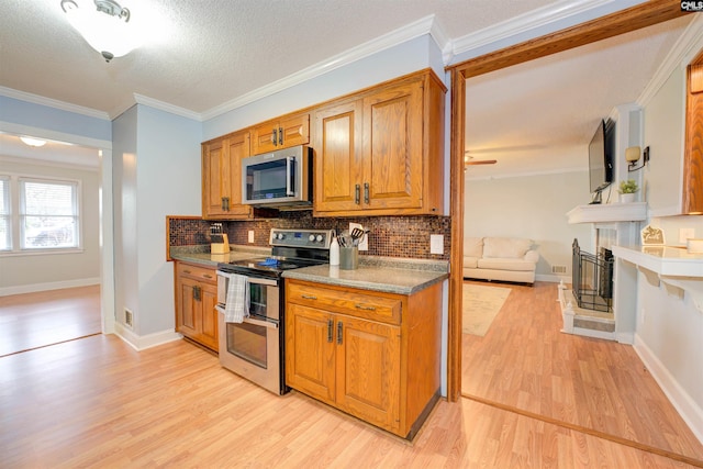 kitchen featuring light wood-style flooring, a fireplace with raised hearth, appliances with stainless steel finishes, brown cabinets, and backsplash