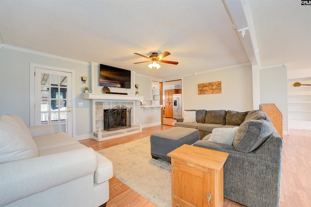 living room featuring ceiling fan, a fireplace, light wood-style flooring, and crown molding