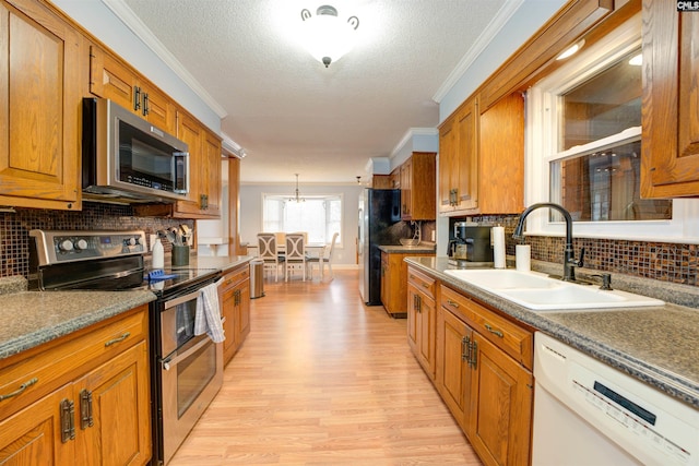 kitchen featuring brown cabinetry, a sink, light wood-style floors, appliances with stainless steel finishes, and crown molding