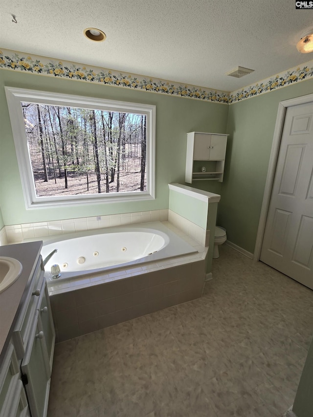 full bathroom with vanity, a tub with jets, visible vents, a textured ceiling, and toilet