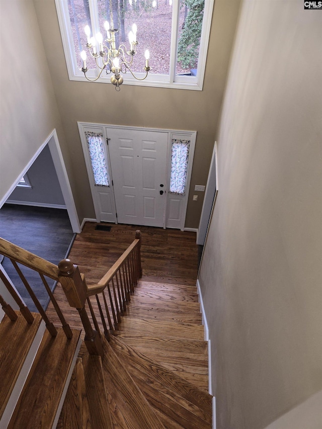 entryway with baseboards, stairs, an inviting chandelier, a towering ceiling, and dark wood-style floors