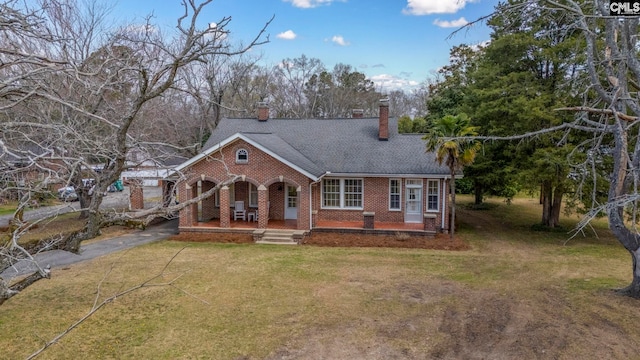 view of front facade with brick siding, a front lawn, aphalt driveway, covered porch, and a chimney