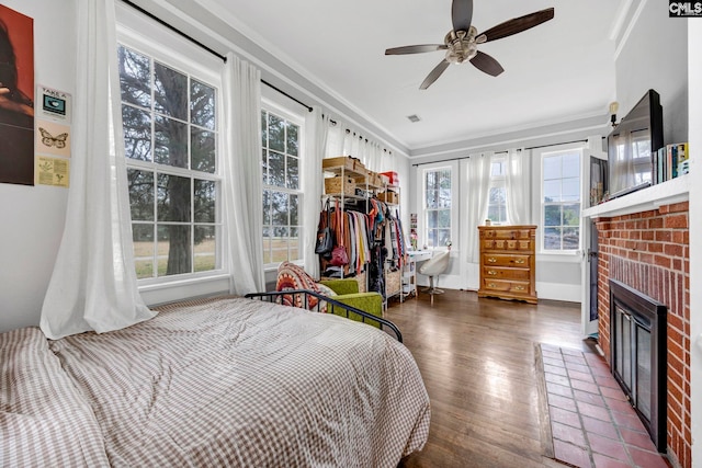 bedroom with crown molding, a brick fireplace, wood finished floors, and visible vents