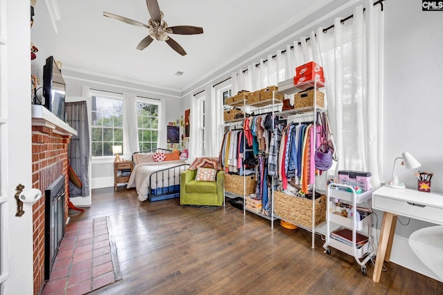 bedroom with a brick fireplace, crown molding, a ceiling fan, and wood finished floors