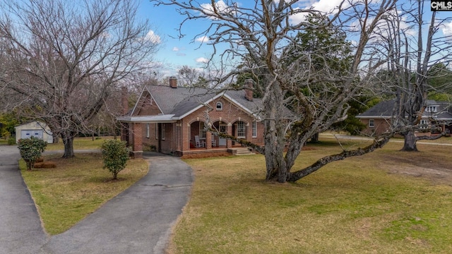 view of front of property with brick siding, a front lawn, aphalt driveway, covered porch, and a chimney