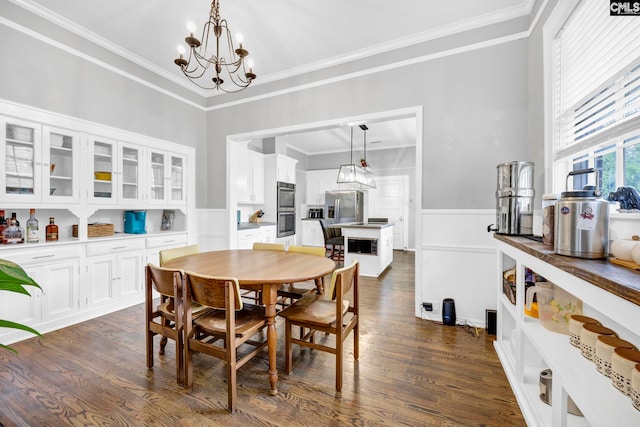 dining room featuring wainscoting, dark wood-type flooring, an inviting chandelier, and ornamental molding