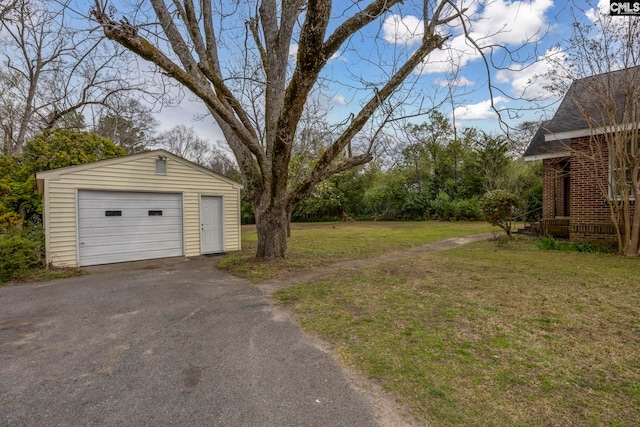 view of yard featuring an outdoor structure, a detached garage, and aphalt driveway