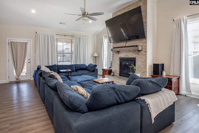 living area with visible vents, a ceiling fan, wood finished floors, a stone fireplace, and vaulted ceiling