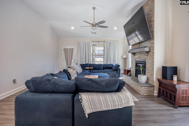 living room with a ceiling fan, vaulted ceiling, a stone fireplace, and wood finished floors