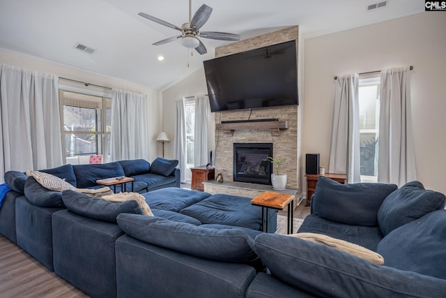 living area featuring visible vents, ceiling fan, lofted ceiling, a stone fireplace, and wood finished floors