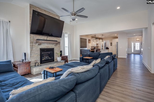 living room featuring a ceiling fan, a stone fireplace, wood finished floors, and baseboards