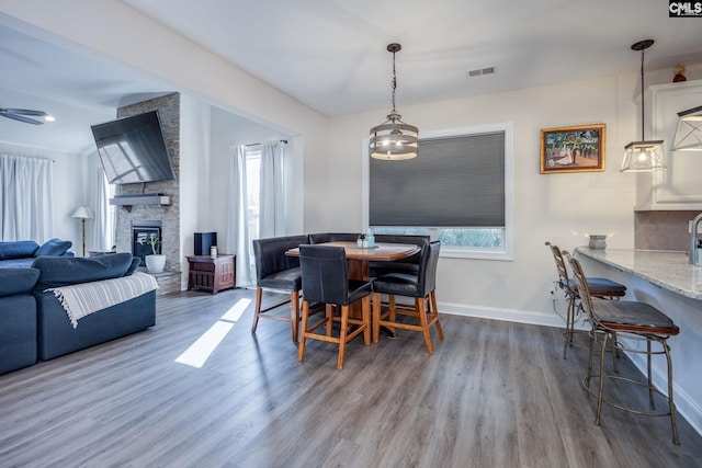 dining area with visible vents, wood finished floors, a fireplace, baseboards, and ceiling fan