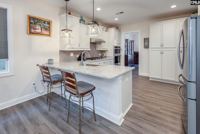 kitchen with visible vents, a sink, decorative backsplash, under cabinet range hood, and appliances with stainless steel finishes