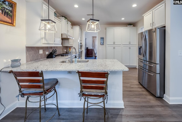 kitchen featuring a peninsula, a sink, stainless steel fridge, white cabinetry, and tasteful backsplash