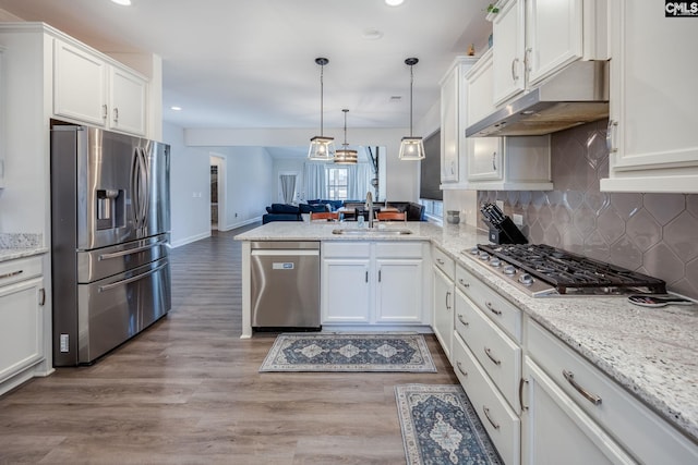 kitchen featuring a sink, under cabinet range hood, open floor plan, stainless steel appliances, and a peninsula