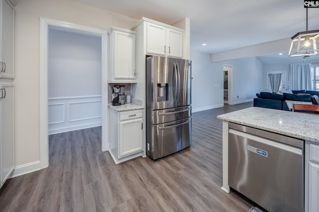 kitchen featuring light stone countertops, light wood-style flooring, stainless steel appliances, white cabinets, and open floor plan