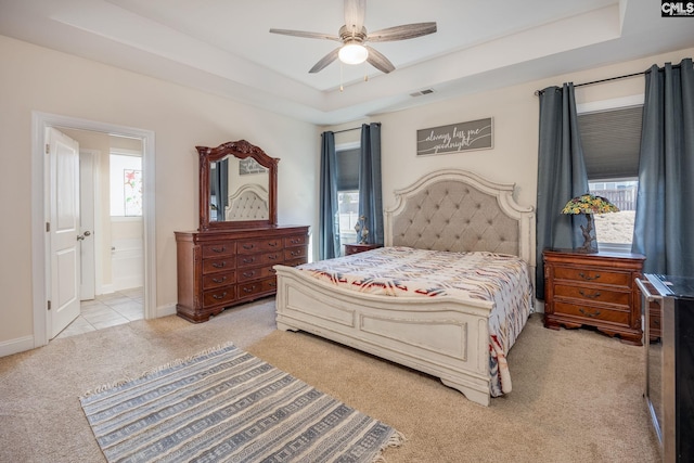 bedroom featuring a tray ceiling, light colored carpet, visible vents, and baseboards