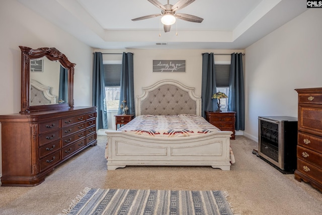 bedroom with ceiling fan, a tray ceiling, light carpet, and beverage cooler