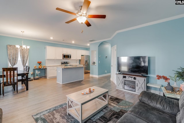 living room featuring crown molding, baseboards, ceiling fan with notable chandelier, light wood-style floors, and arched walkways