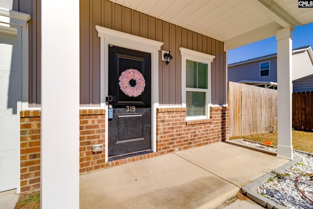 view of exterior entry featuring brick siding, board and batten siding, and fence