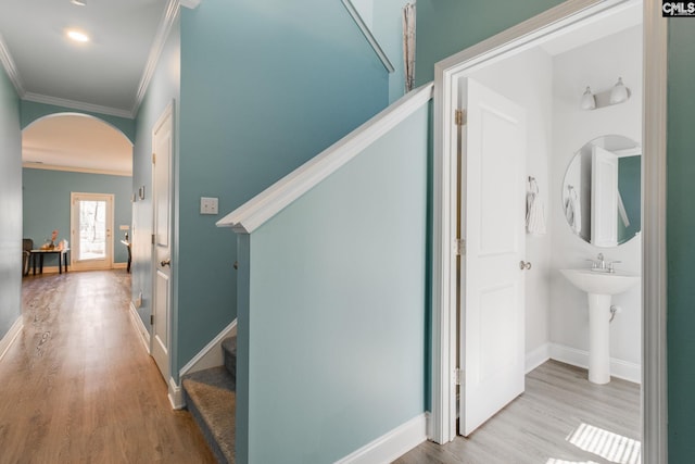 hallway with baseboards, stairs, ornamental molding, wood finished floors, and arched walkways