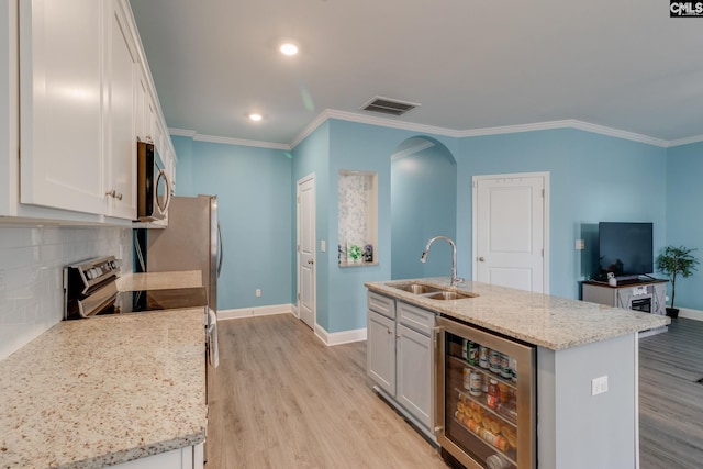 kitchen with beverage cooler, light wood-type flooring, appliances with stainless steel finishes, arched walkways, and a sink