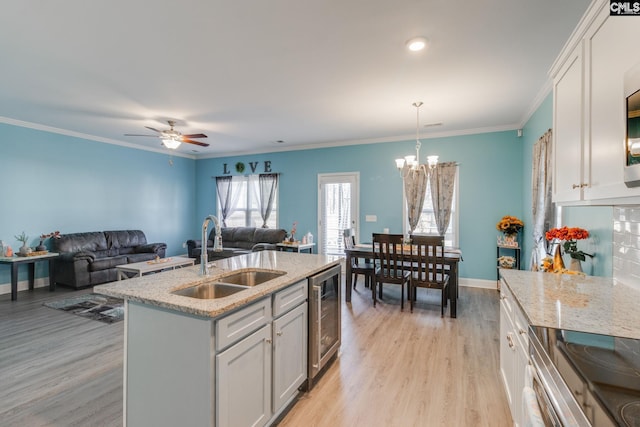 kitchen with wine cooler, white cabinets, light wood finished floors, and a sink