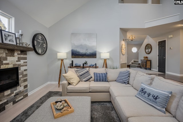 living area with a fireplace, stairway, wood finished floors, and high vaulted ceiling