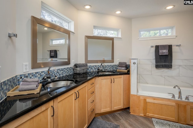 bathroom with double vanity, a bath, wood finished floors, and a sink